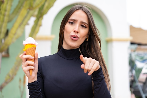 Jonge mooie vrouw met een cornet-ijs naar buiten verrast en wijzend naar voren