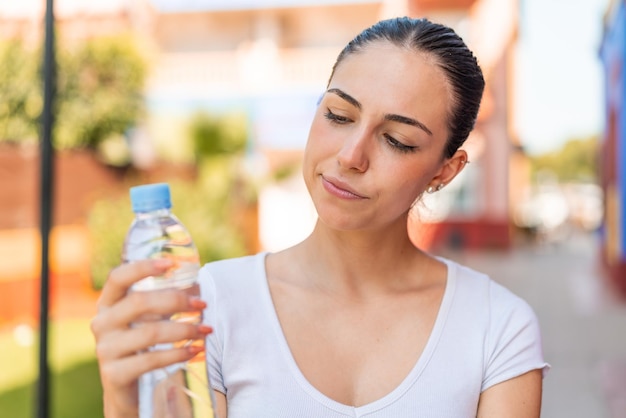 Foto jonge mooie vrouw met een fles water in de buitenlucht met droevige uitdrukking