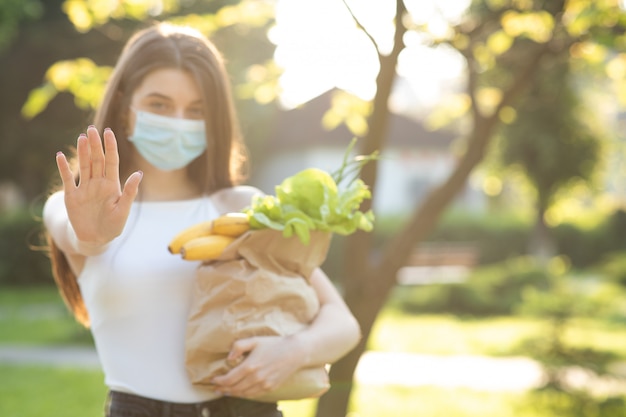 Jonge mooie vrouw met een gezichtsmasker in het park met boodschappen