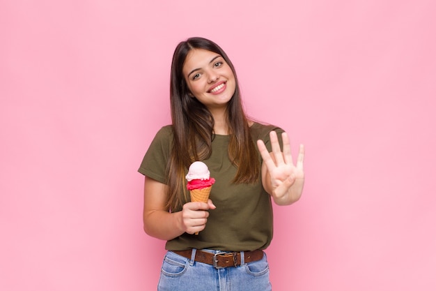Jonge mooie vrouw met een ijsje dat vriendelijk glimlacht en kijkt, nummer vier of vierde met vooruit hand toont, aftellend
