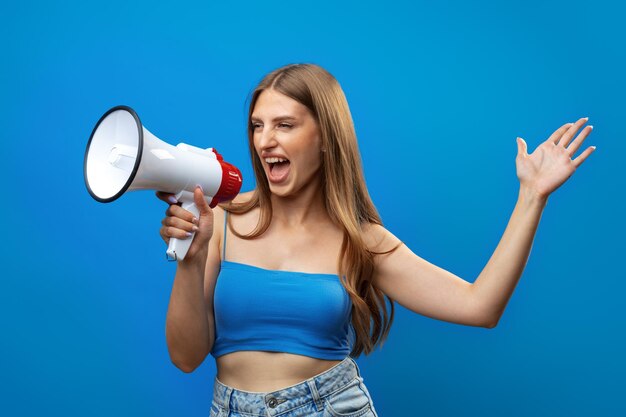 Jonge mooie vrouw met een megafoon op blauwe achtergrond in de studio