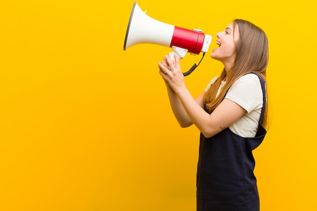 Jonge mooie vrouw met een megafoon tegen oranje achtergrond