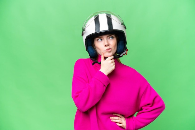 Jonge mooie vrouw met een motorhelm over geïsoleerde chroma key achtergrond met twijfels