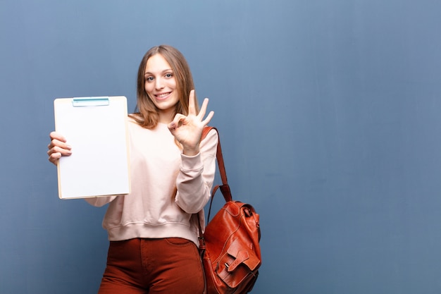 Jonge mooie vrouw met een stuk papier tegen blauwe muur met een kopie ruimte