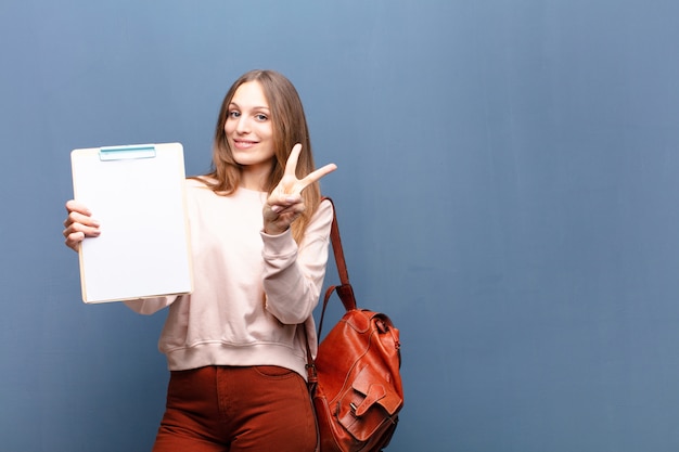 Jonge mooie vrouw met een stuk papier tegen blauwe muur