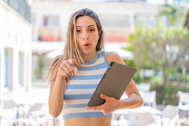 Foto jonge mooie vrouw met een tablet buitenshuis verrast en wijzend naar voren