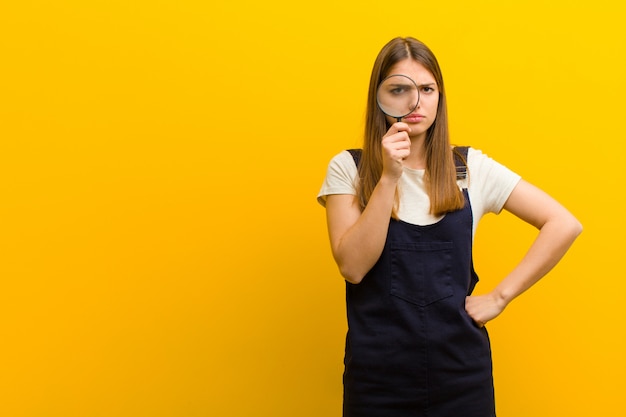 Jonge mooie vrouw met een vergrootglas tegen sinaasappel