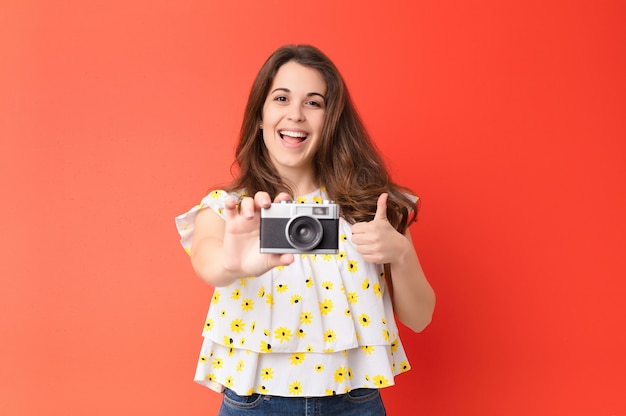 Jonge mooie vrouw met een vintage camera over rode muur