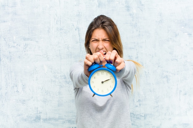 Jonge mooie vrouw met een wekker op grungemuur