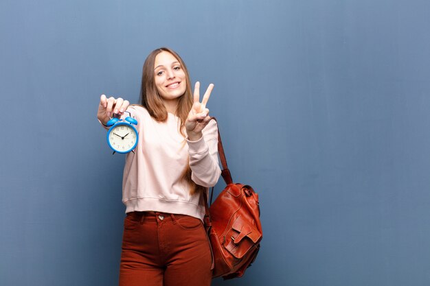 Jonge mooie vrouw met een wekker tegen blauw met een copyspace