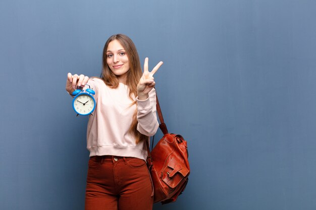 Jonge mooie vrouw met een wekker tegen blauwe muur met een exemplaarruimte