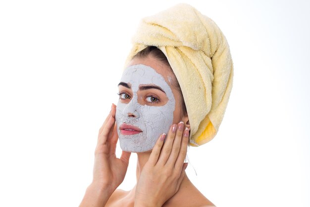 Jonge mooie vrouw met gele handdoek op haar hoofd en cosmetisch masker op haar gezicht met witte bloem