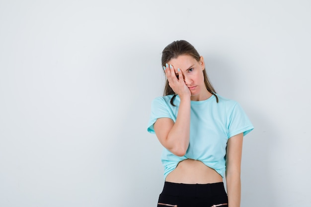 Jonge mooie vrouw met hand op gezicht in t-shirt en geïrriteerd, vooraanzicht.