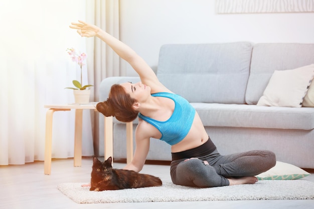 Jonge mooie vrouw met kat die thuis yoga beoefent