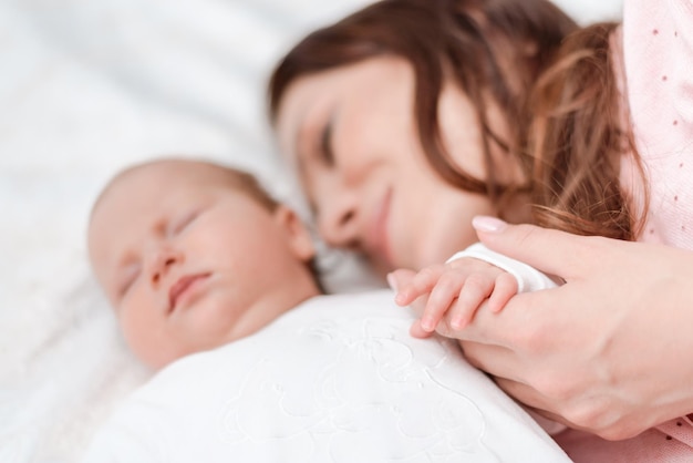 Jonge mooie vrouw met kleine hand van haar slapende babydochter in slaapkamer