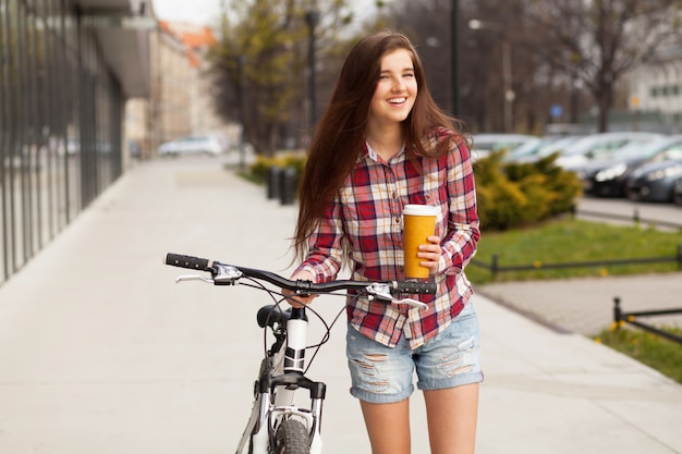 Jonge mooie vrouw met koffiekopje en een fiets