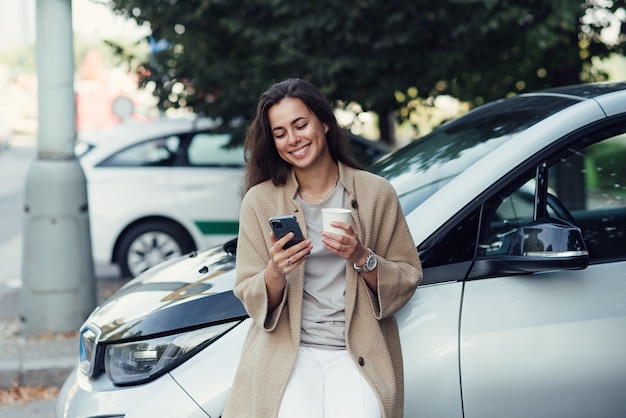 Jonge mooie vrouw met kopje koffie en sms-blog op tablet in herfstpark in de buurt van voertuig