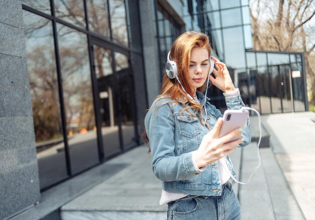 Jonge mooie vrouw met koptelefoon en met een smartphone in de buurt van het zakencentrum