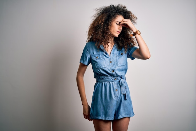 Jonge mooie vrouw met krullend haar en piercing dragen casual denim jurk moe wrijven neus en ogen gevoel van vermoeidheid en hoofdpijn Stress en frustratie concept