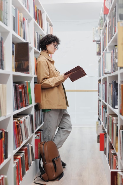 Jonge mooie vrouw met krullend haar in de bibliotheek tussen de planken met boeken een studente voert wetenschappelijk werk uit