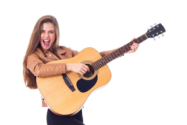 Jonge mooie vrouw met lang haar in jas en zwarte broek die een gitaar vasthoudt en gezichten trekt