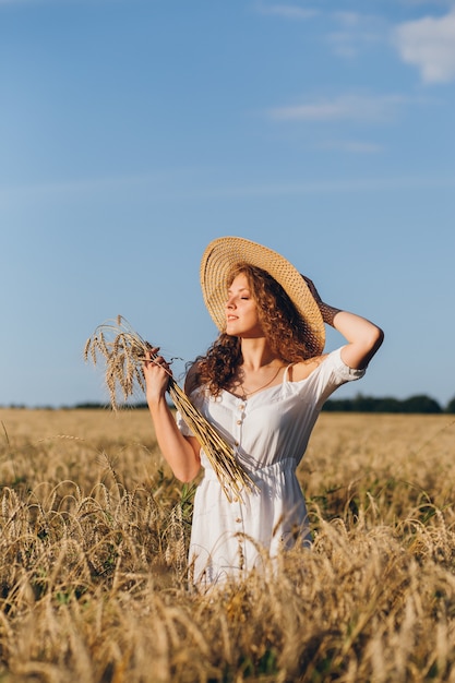 Jonge mooie vrouw met lang krullend haar vormt in een tarweveld in de zomer bij zonsondergang