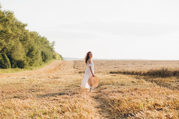 Jonge mooie vrouw met lang krullend haar vormt in een tarweveld in de zomer bij zonsondergang