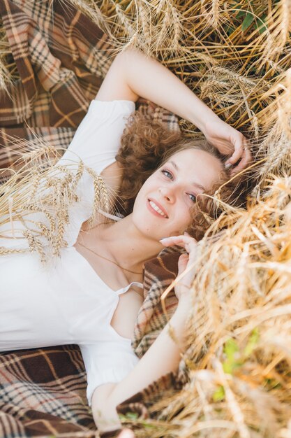 Jonge mooie vrouw met lang krullend haar vormt in een tarweveld in de zomer bij zonsondergang