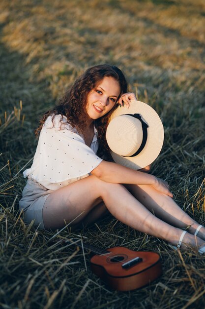 Jonge mooie vrouw met lang krullend haar vormt in een tarweveld in de zomer bij zonsondergang