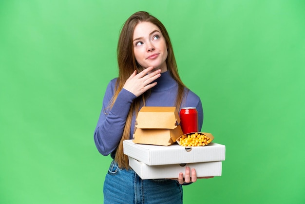 Jonge mooie vrouw met pizza's en hamburgers over geïsoleerde chroma key achtergrond terwijl ze glimlacht