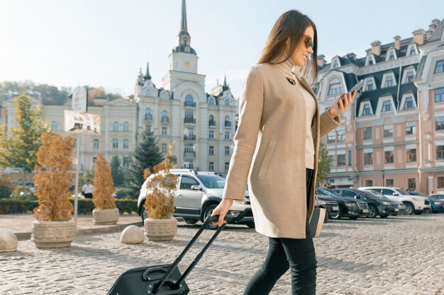 Jonge mooie vrouw met reiskoffer en mobiele telefoon