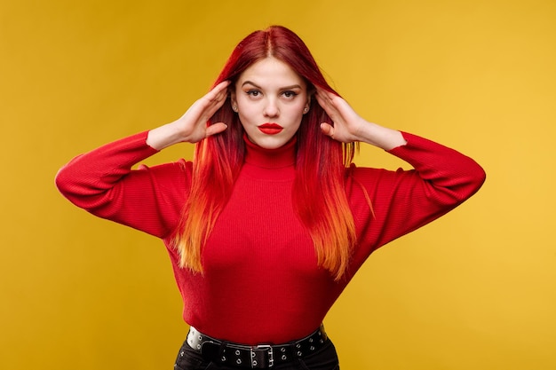 Jonge mooie vrouw met rood haar en rode sweter die zich voordeed op gele achtergrond