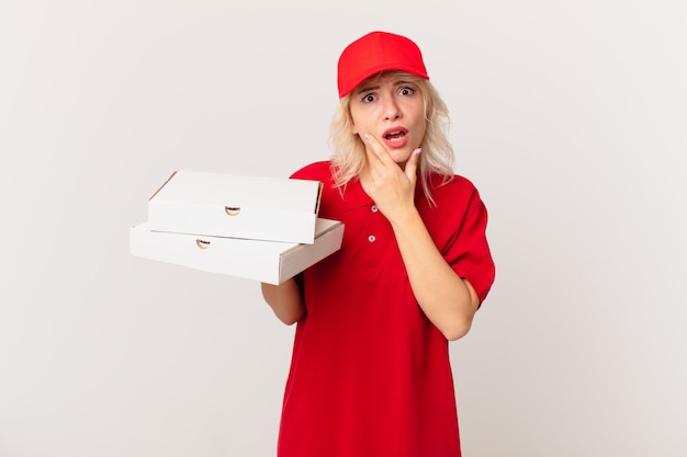 Jonge mooie vrouw met wijd open mond en ogen en hand op kin. pizza bezorgconcept