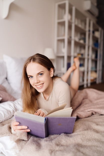 Jonge mooie vrouw op bed thuis genieten van favoriete boek