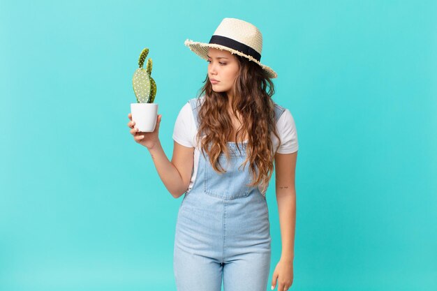 Jonge mooie vrouw op profielweergave denkend of dagdromend en een cactus vasthoudend