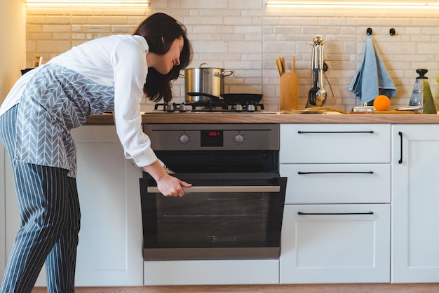 Jonge mooie vrouw open oven om binnenlands keukenconcept te koken