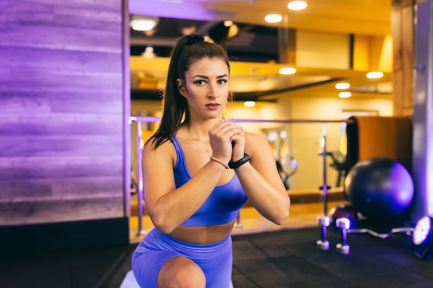 Jonge mooie vrouw opwarmt en strekt zich uit in de sportschool op een mat in de buurt van de spiegel in een blauw pak