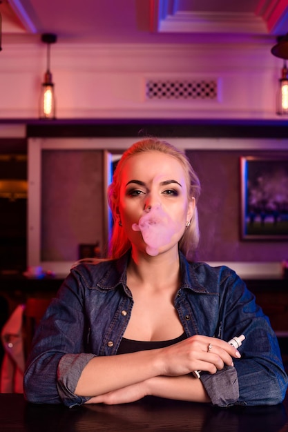 Jonge mooie vrouw rookt een elektronische sigaret aan de vape-bar