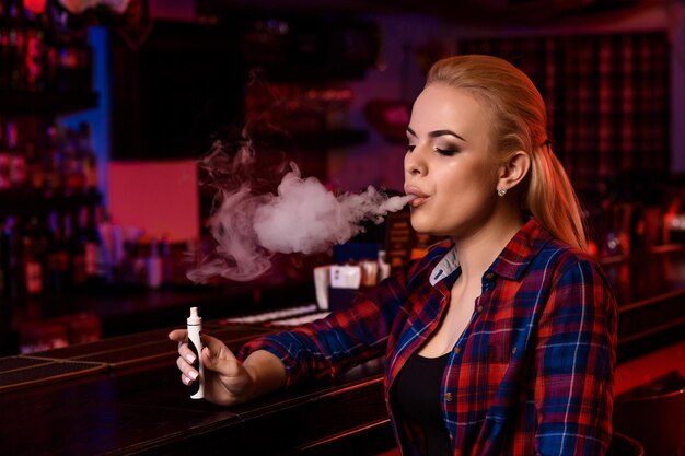 Jonge mooie vrouw rookt een elektronische sigaret aan de vape-bar