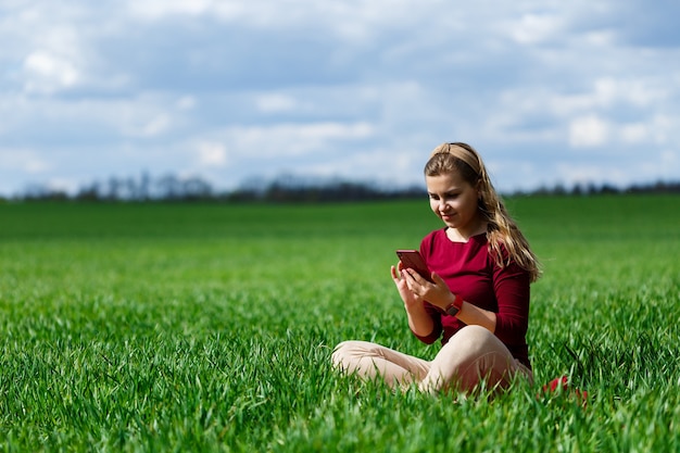 Jonge mooie vrouw student met een telefoon in haar handen zittend op het gras. Meisje neemt selfies en maakt selfie-foto's. Ze lacht en geniet van een warme dag. Conceptfoto op smartphone