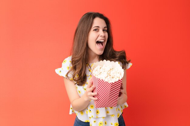 Jonge mooie vrouw tegen rode muur met een popcornemmer