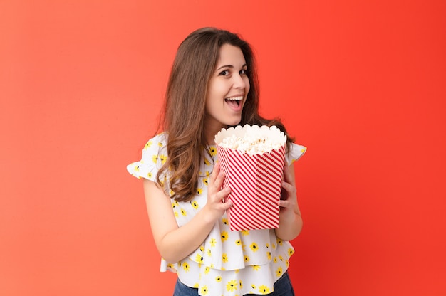 Jonge mooie vrouw tegen rode muur met een popcornemmer