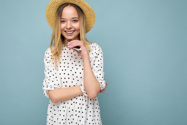 Jonge mooie vrouw. Trendy vrouw in casual zomerjurk en strohoed. Positieve vrouw toont gezichtsemoties. Grappig model geïsoleerd op blauwe achtergrond met vrije ruimte.