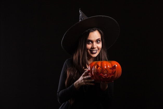 Jonge mooie vrouw verkleed als een heks voor Halloween. Jong met het houden van een pompoen. Heks glimlachen.