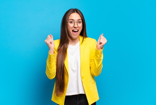 Foto jonge mooie vrouw voelt zich geschokt, opgewonden en gelukkig, lacht en viert succes en zegt wow!