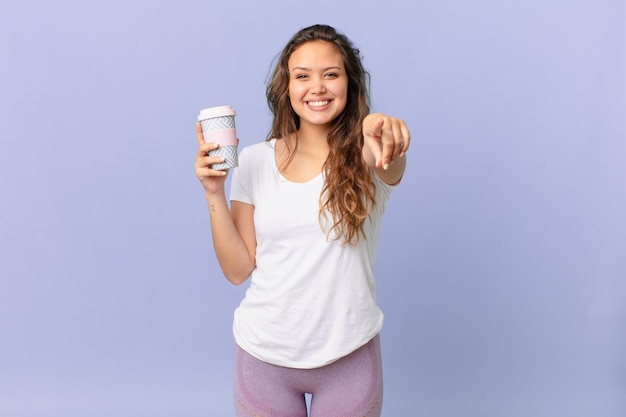 Jonge mooie vrouw wijzend op de camera die jou kiest en een kopje koffie houdt