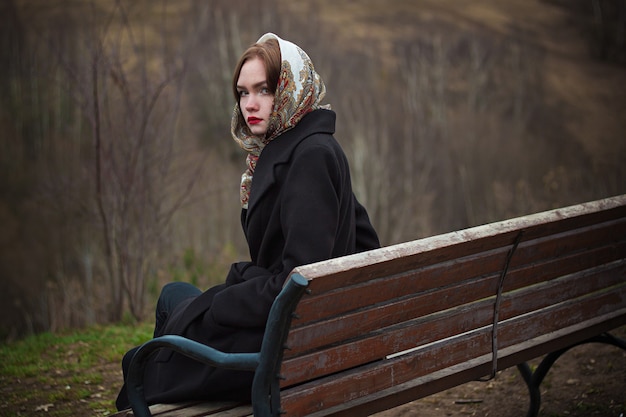 jonge mooie vrouw zit op een bankje in de herfst in de natuur en kijkt over haar schouder.