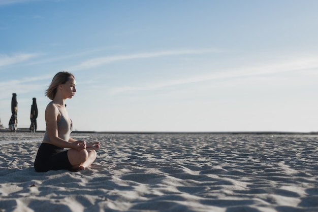 Jonge mooie vrouw zit op het zand en mediteert