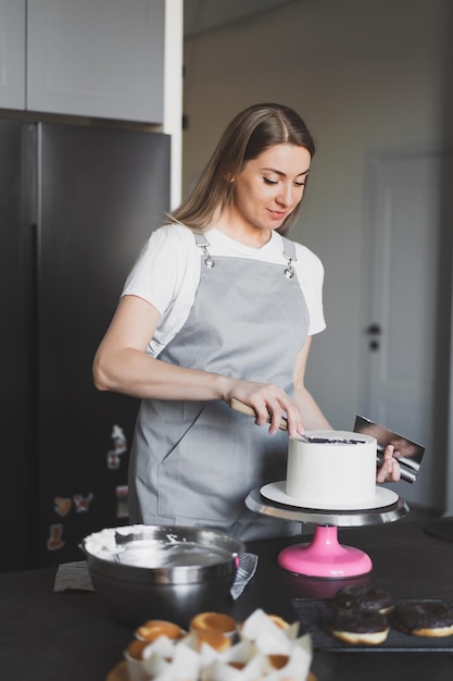 Jonge mooie vrouwelijke banketbakker die een feestelijke cake thuis in de keuken voorbereidt