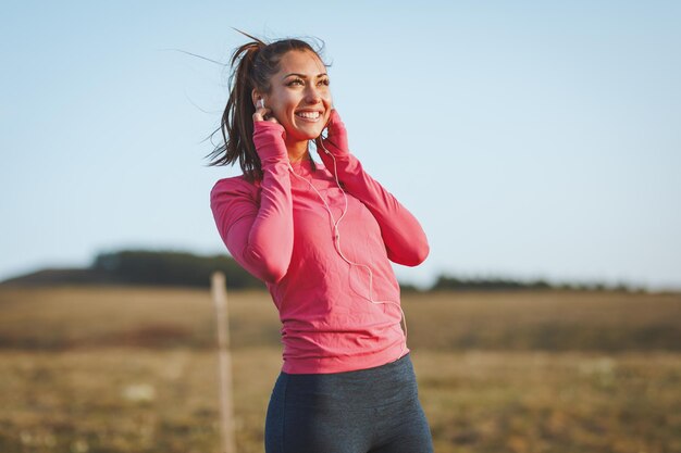 Jonge mooie vrouwelijke hardloper die naar muziek luistert en een pauze neemt na het joggen in de ochtend in de bergen.